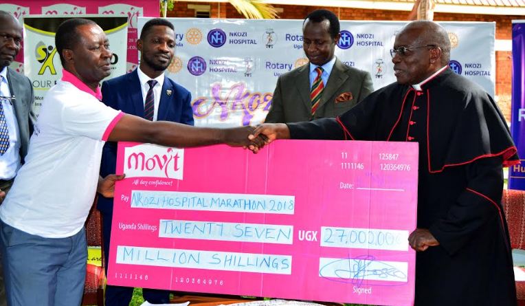 Vicar General of the Kampala archdioceses of Kampala receiving a dummy cheque from Movit's John Tumwesigye