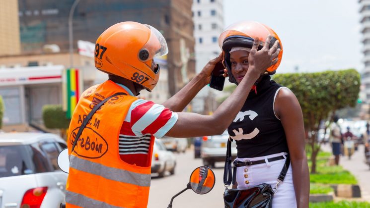 A safeboda rider pictured helping out a young lady with wearing her helmet as she gets ready to take on with the ride. (Photo Courtesy: Quartz)
