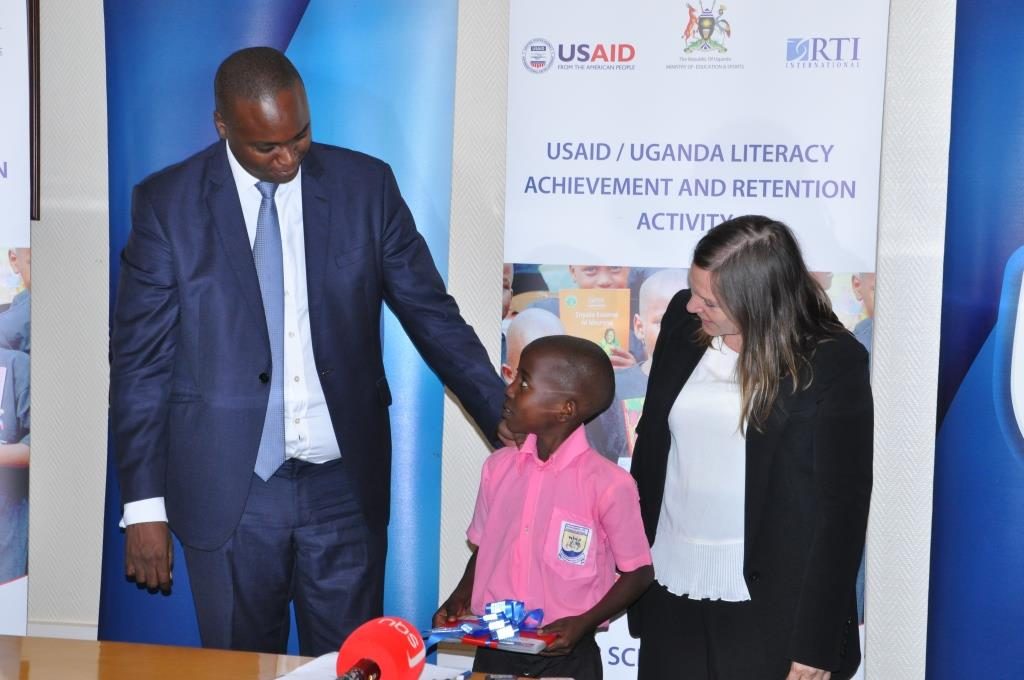 Stanbic Bank Uganda CEO Patrick Mweheire  and USAID Chief of Party Geri Burkholder officially handover reading cards to Kenneth Kivumbi a P.3 pupil from Bamusuta Primary School, one of the beneficiaries of the cards in Kiboga district.